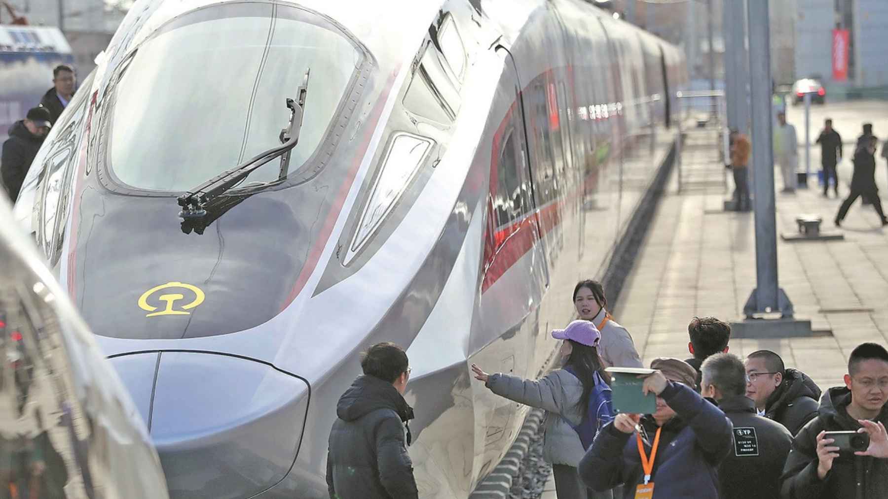 A sleek, white CR450 high-speed bullet train with a red stripe stopped at a platform while passengers take photos.
