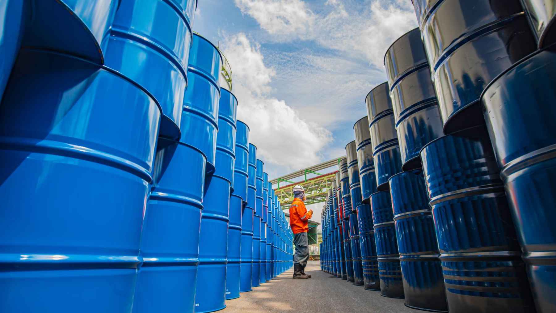 Worker inspecting rows of oil barrels at an industrial storage facility amid tensions over European energy supply and Russian oil transit