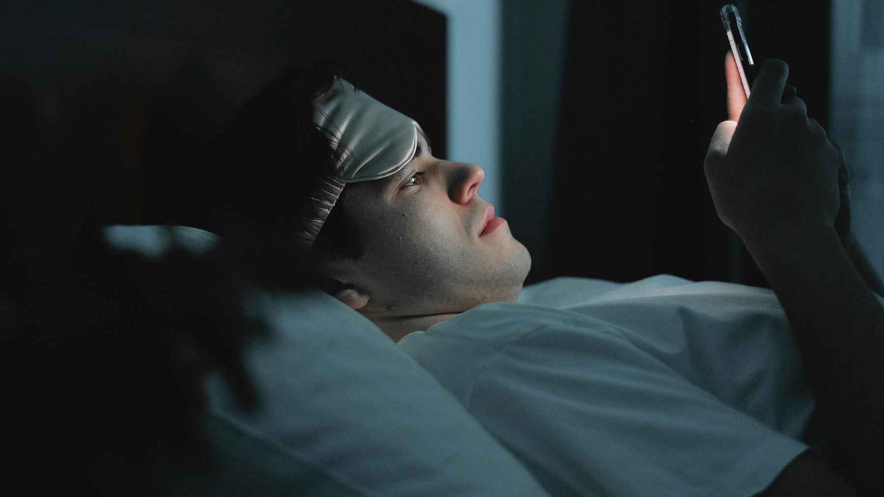 Person using a smartphone in bed at night while looking at the screen before going to sleep.