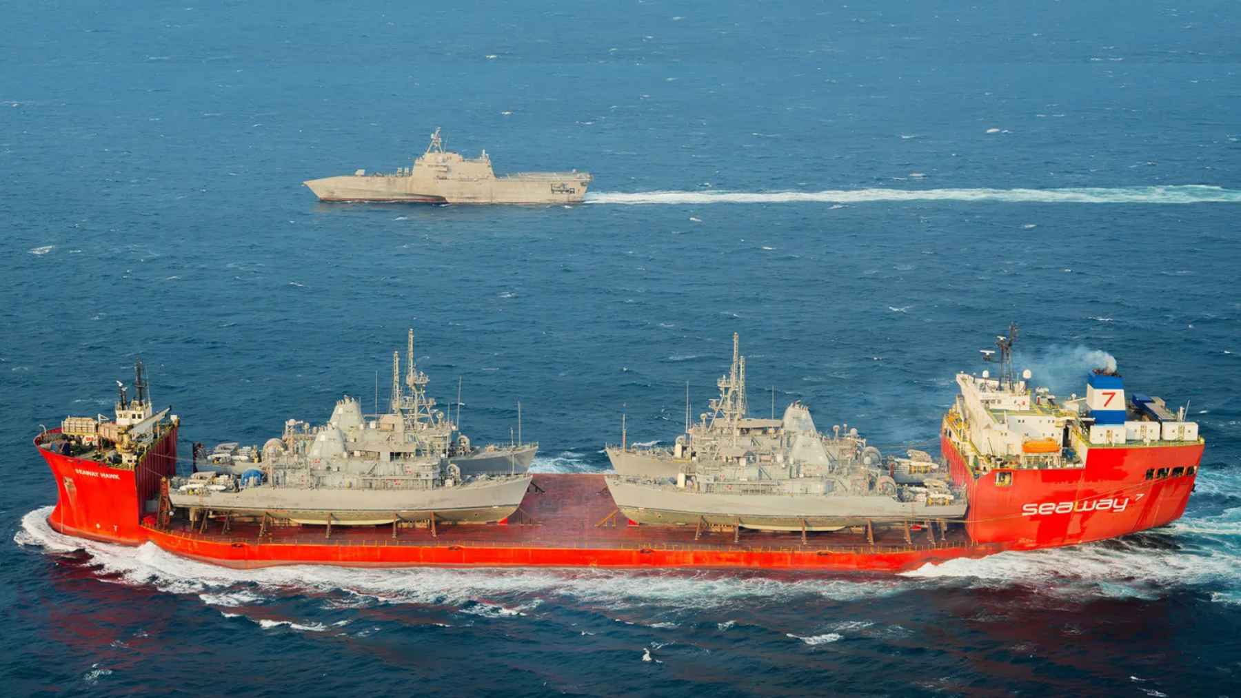 Commercial transport ship carrying military vessels at sea, illustrating the security and shipping tensions tied to the Strait of Hormuz