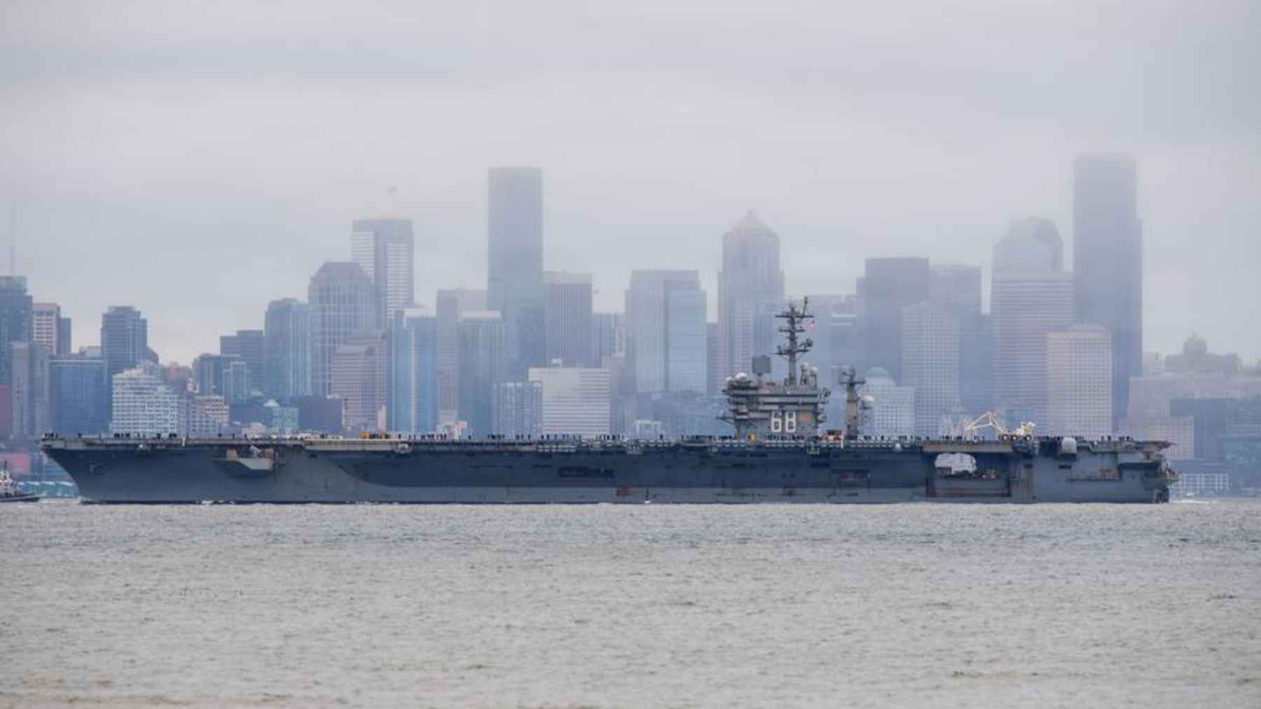 USS Nimitz aircraft carrier sailing near a coastal city skyline during deployment toward South America