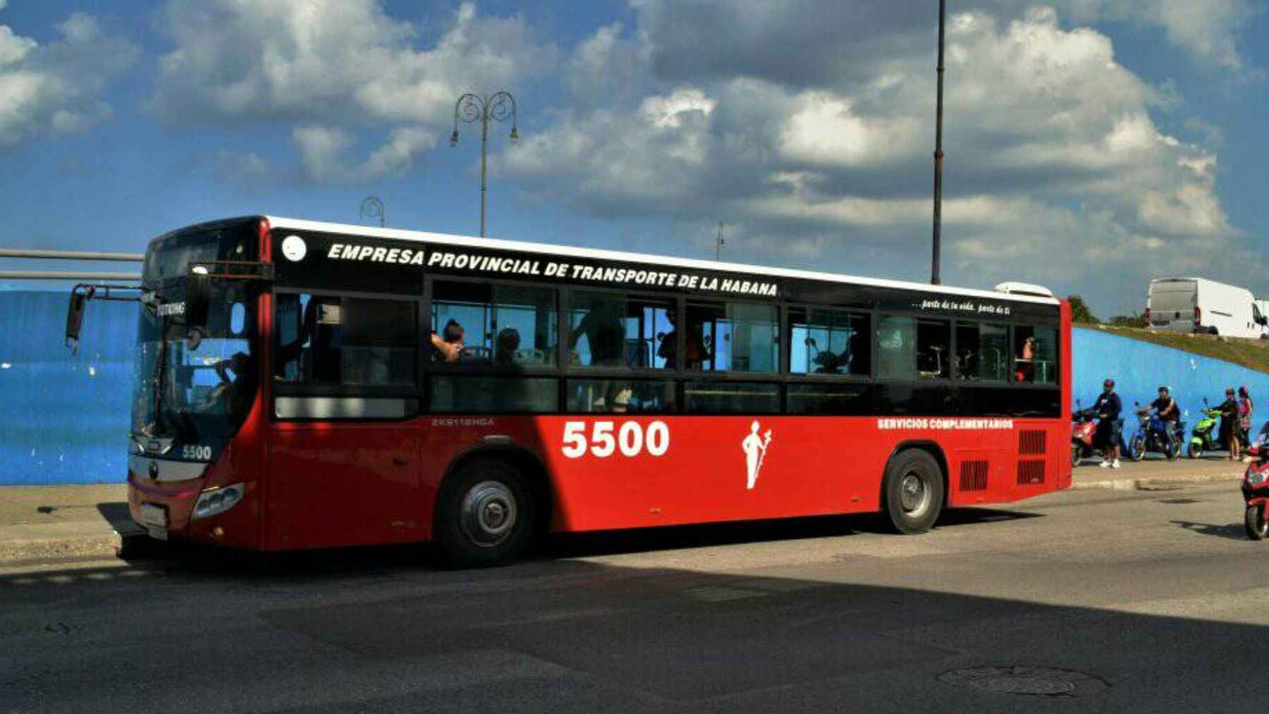 Red public bus in Havana operating during Cuba fuel crisis as scooters and people wait nearby