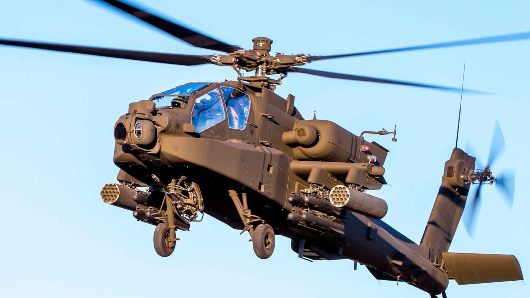 An AH-64 Apache attack helicopter in flight against a clear blue sky, illustrating the manned platforms Japan is moving to retire.