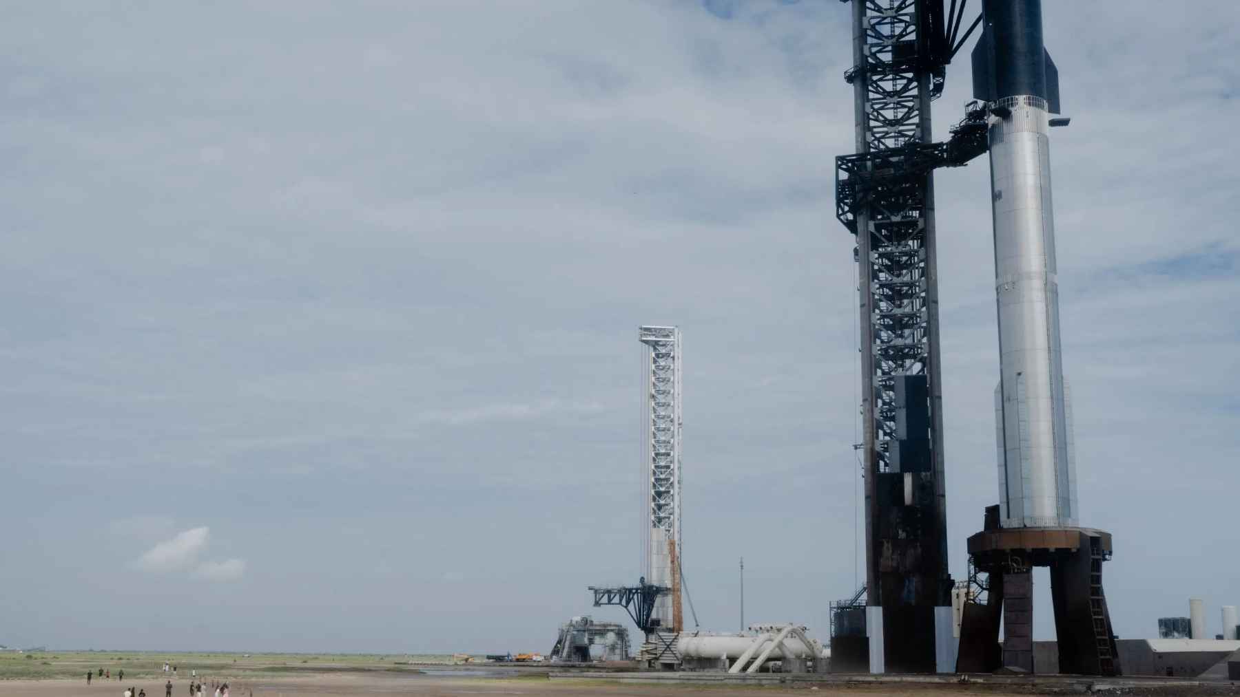 SpaceX Starship rocket and launch tower at Starbase in Texas with visitors walking across the site