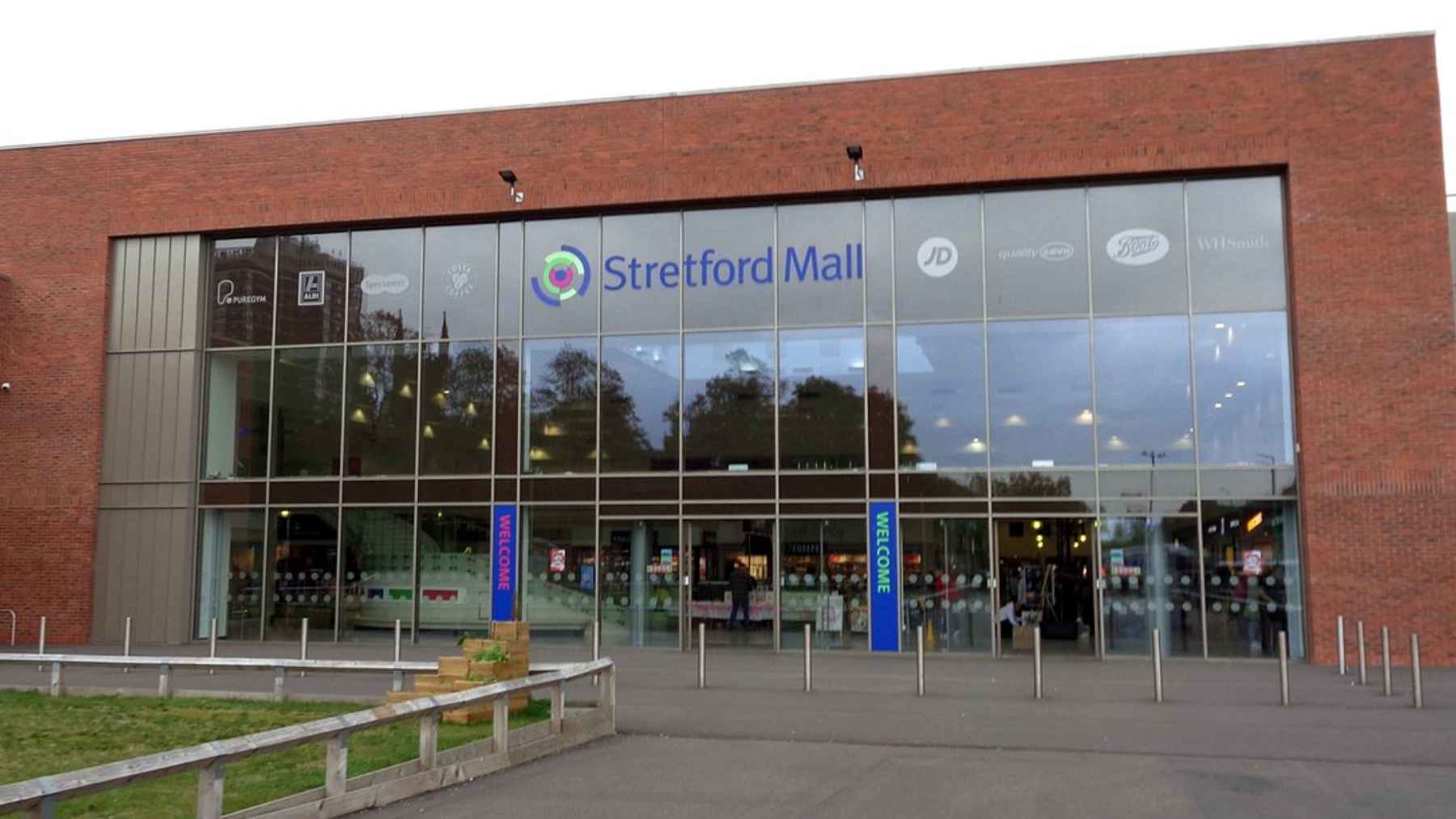 The main exterior entrance of Stretford Mall, featuring red brickwork and large glass windows with "Stretford Mall" signage above the doors.