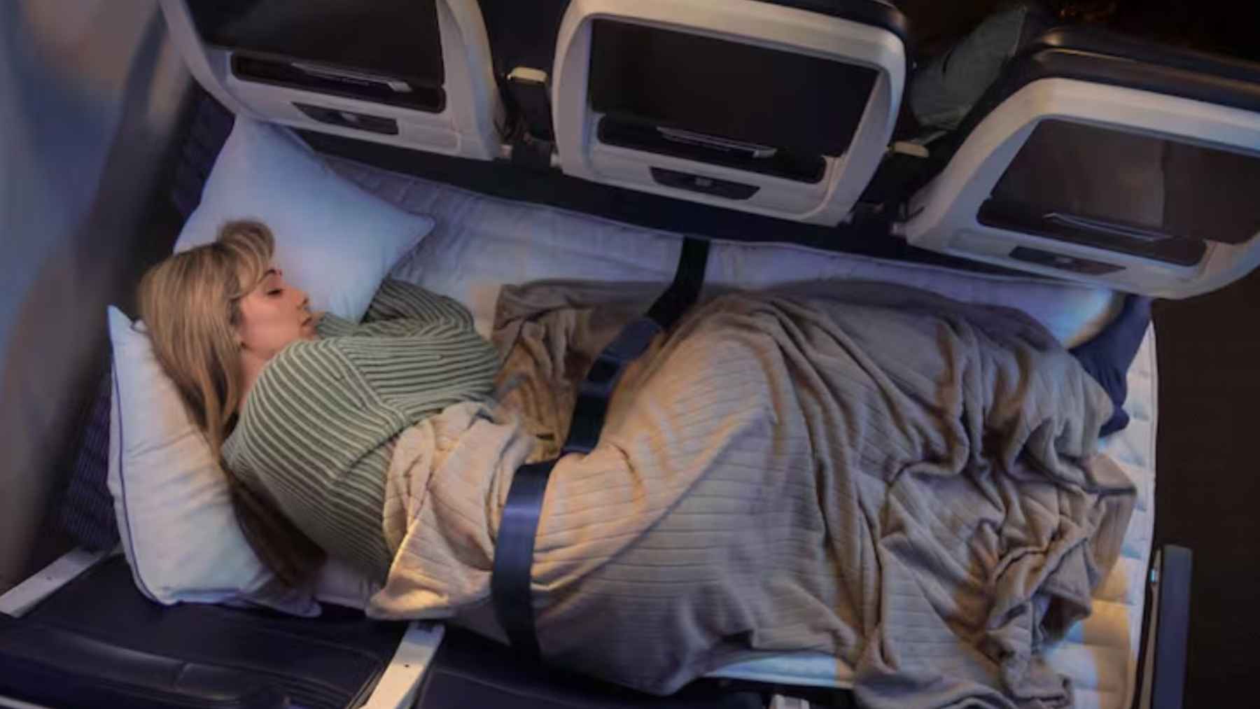 A passenger lying down across three economy seats converted into a flat bed using United Airlines Relax Row bedding and a special seatbelt.