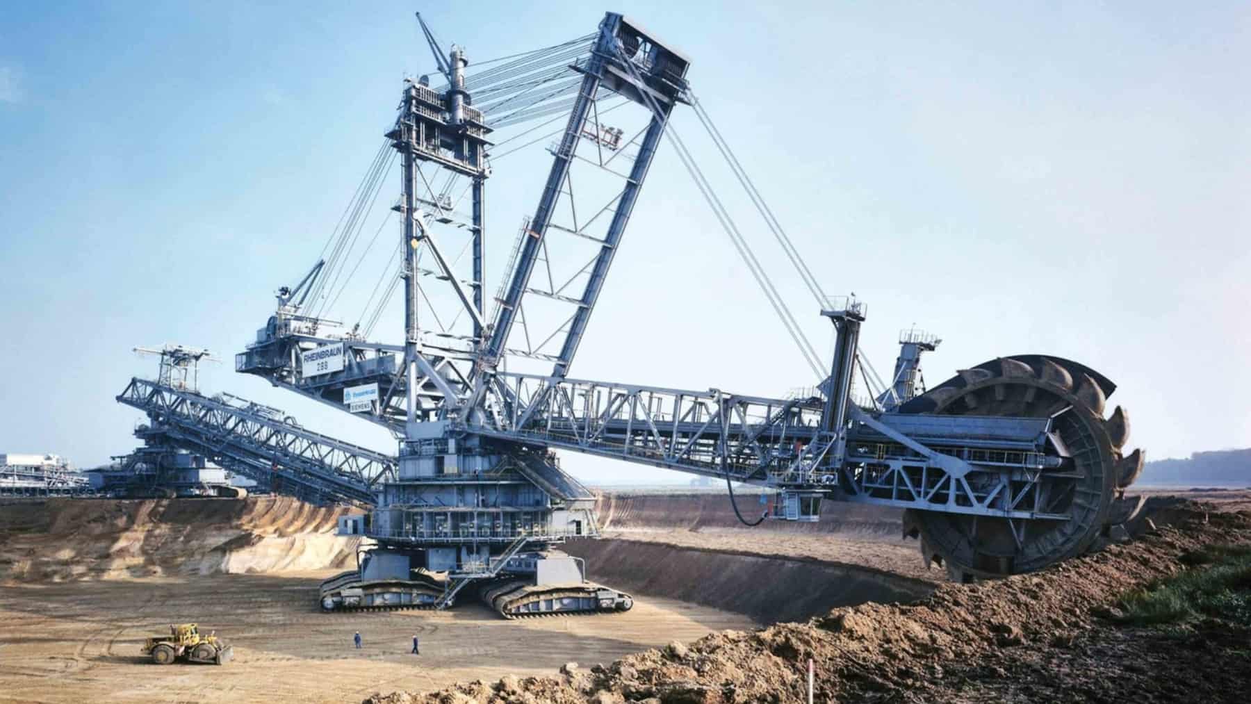 Gran excavadora rotativa de rueda de cangilones trabajando en una mina a cielo abierto, con terreno excavado y maquinaria al fondo.