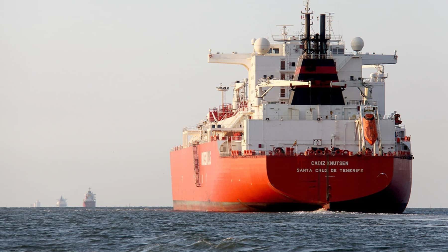 Buque carguero navegando por el mar visto desde la popa con otras embarcaciones al fondo.