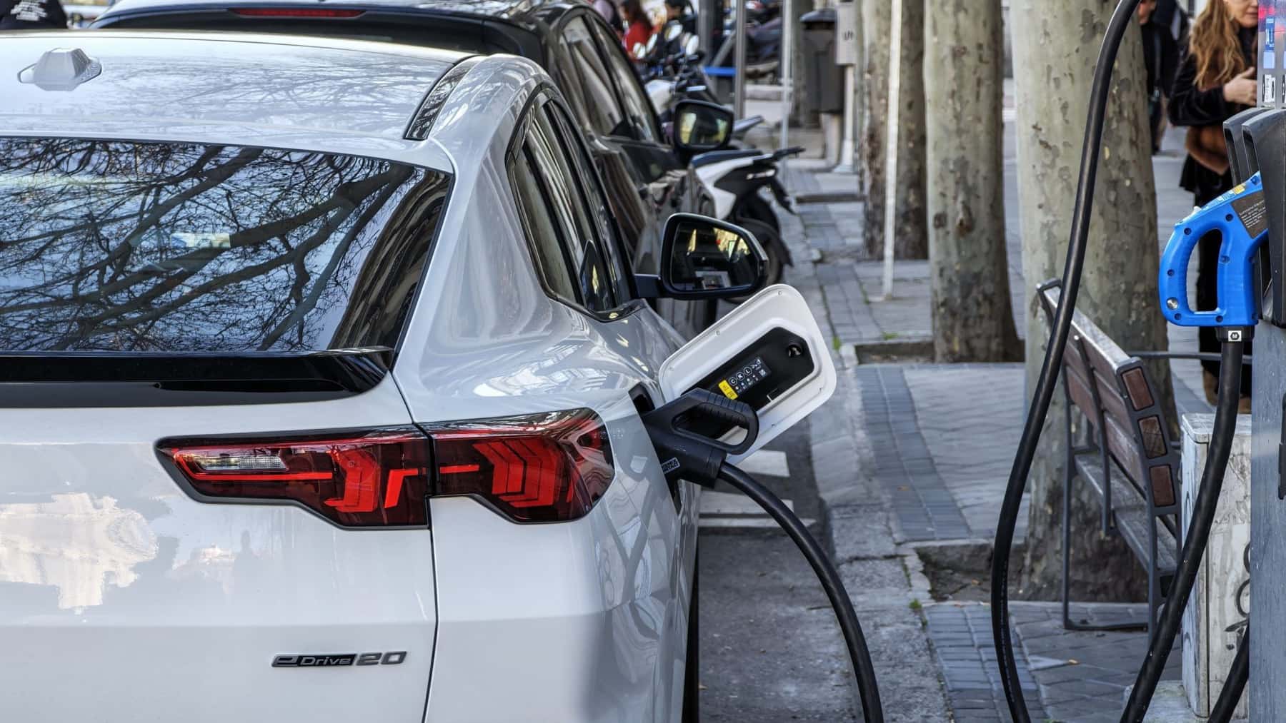 Coche eléctrico blanco cargando batería en un punto de recarga en la calle