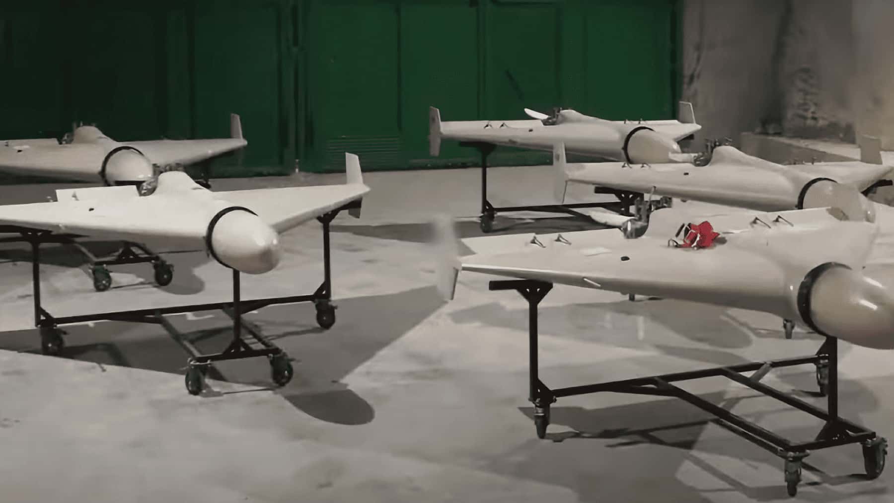 Varios drones iraníes de ala fija colocados sobre soportes en un almacén o instalación militar.
