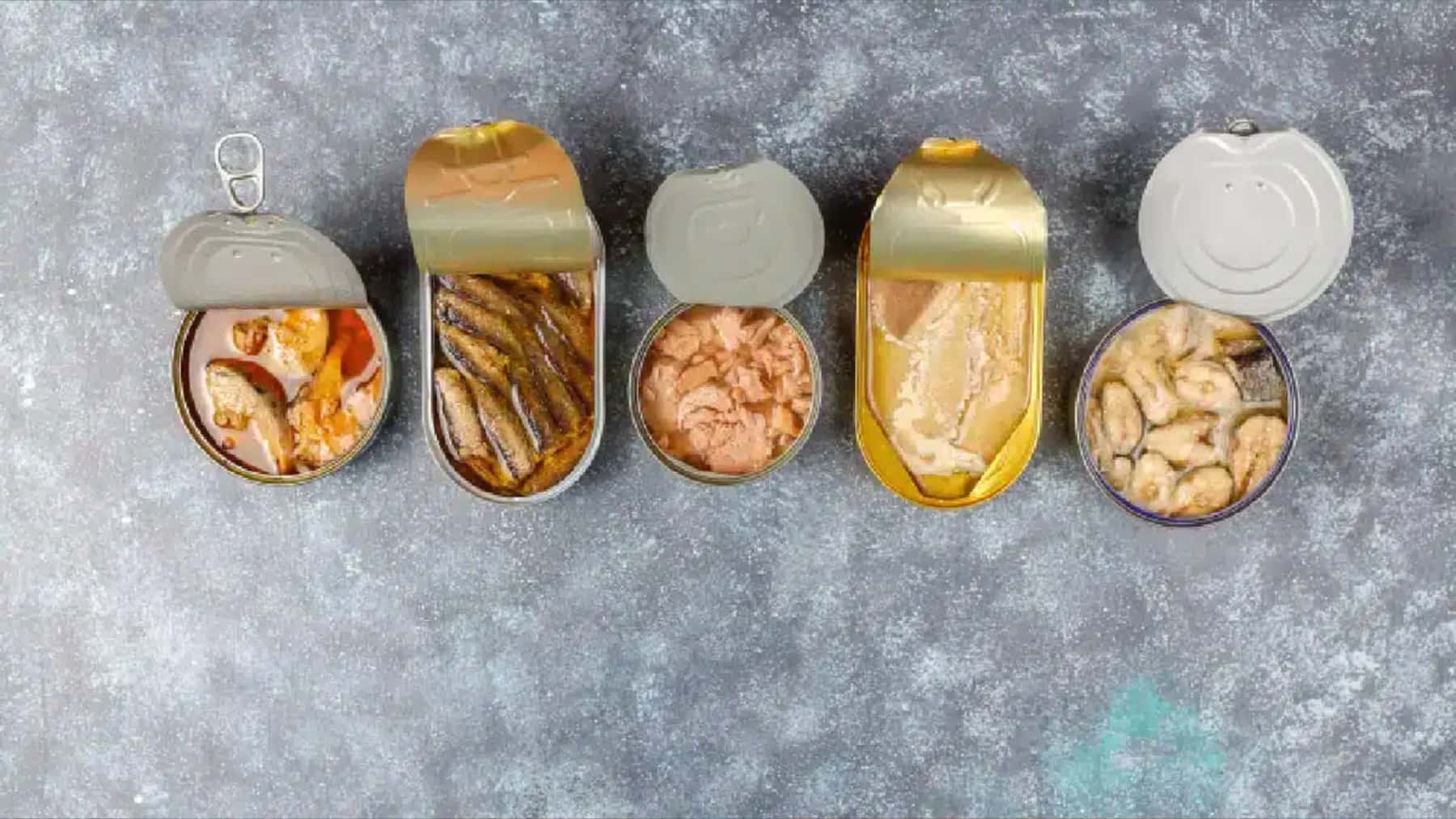 Varias latas abiertas de conservas de pescado y marisco sobre una superficie gris