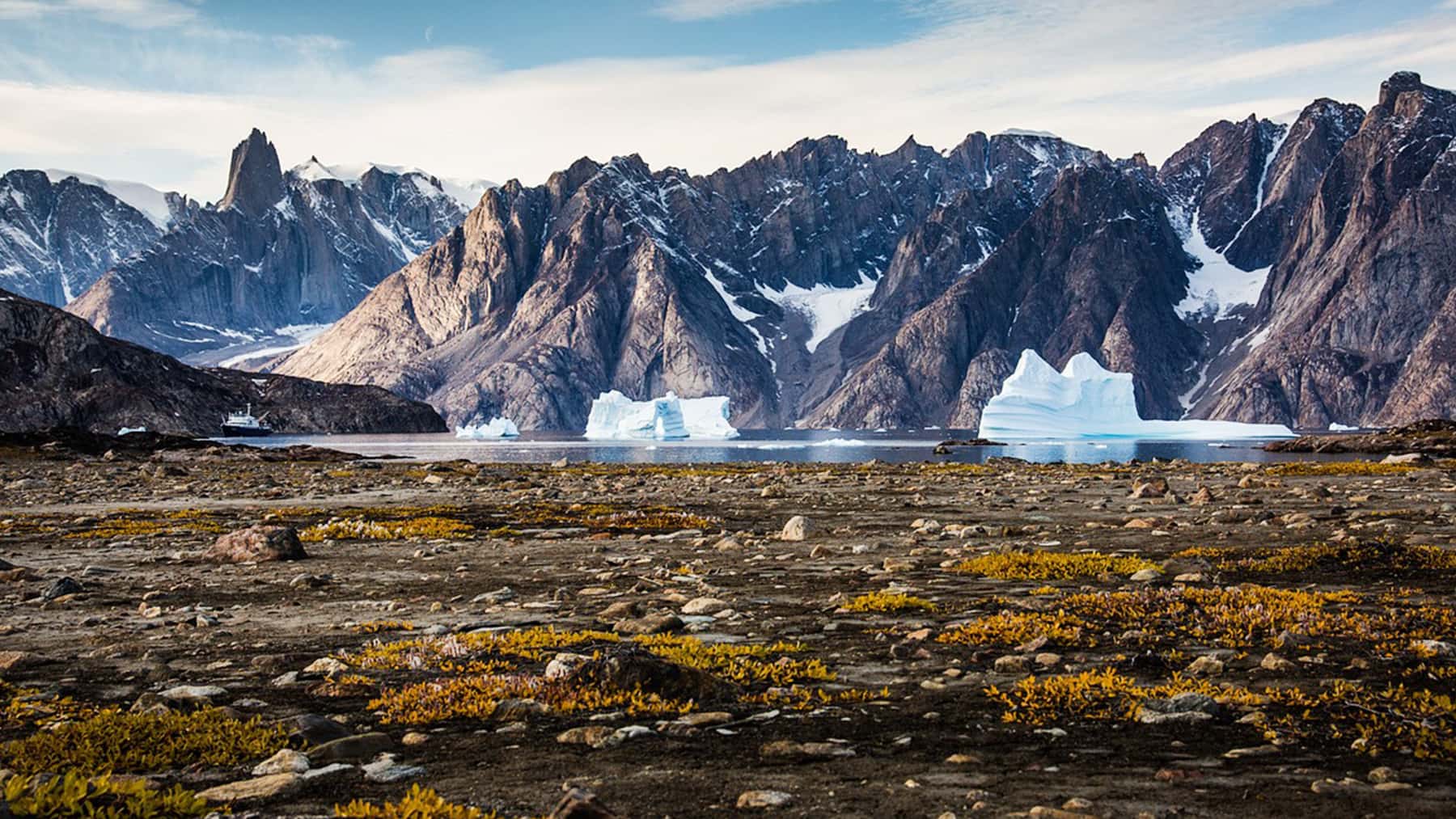 Paisaje del Ártico con montañas escarpadas, glaciares y grandes bloques de hielo flotando en el mar.
