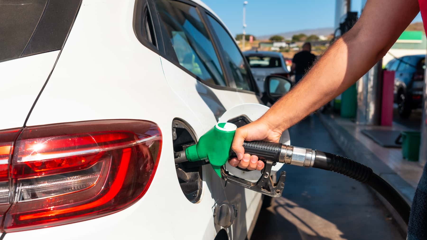 Persona repostando gasolina en un coche blanco en una gasolinera