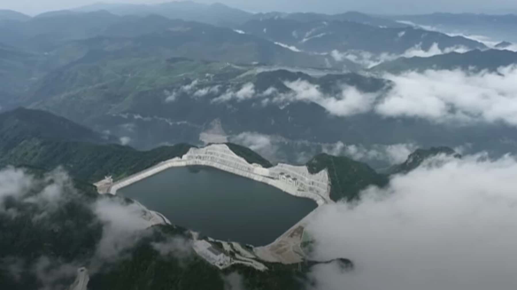 Vista aérea de una presa con embalse rodeado de montañas y nubes bajas