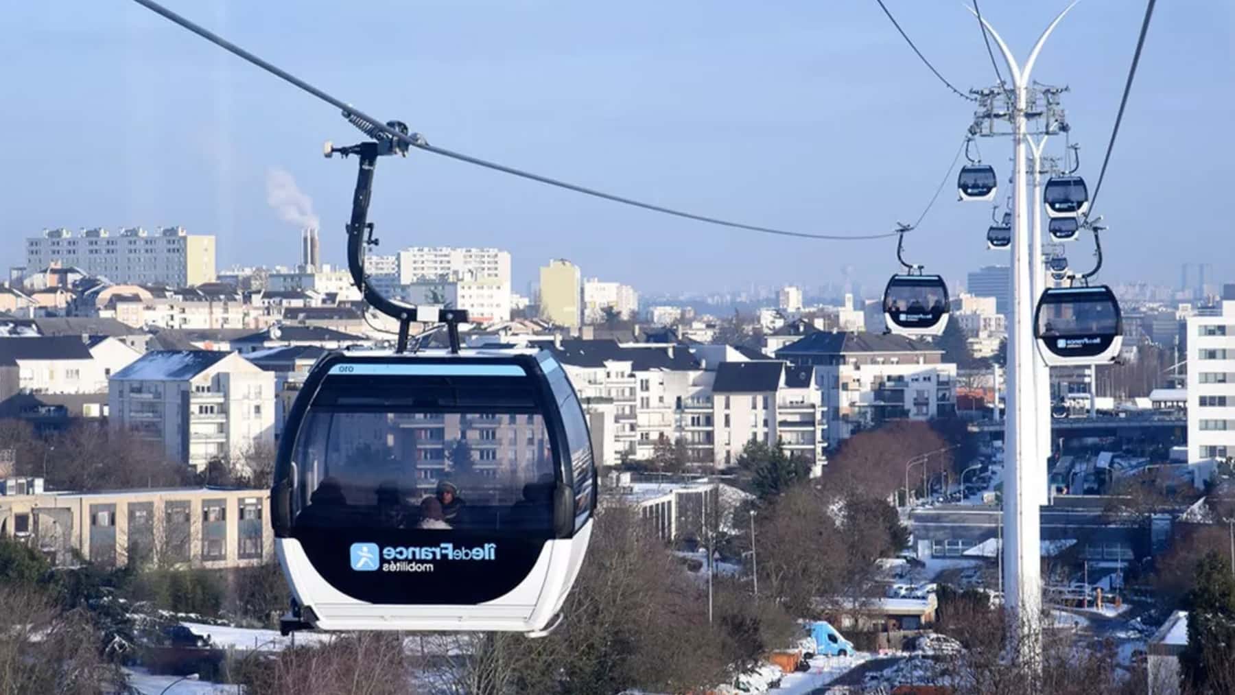 Teleférico urbano con varias cabinas sobrevolando una ciudad entre edificios y calles.