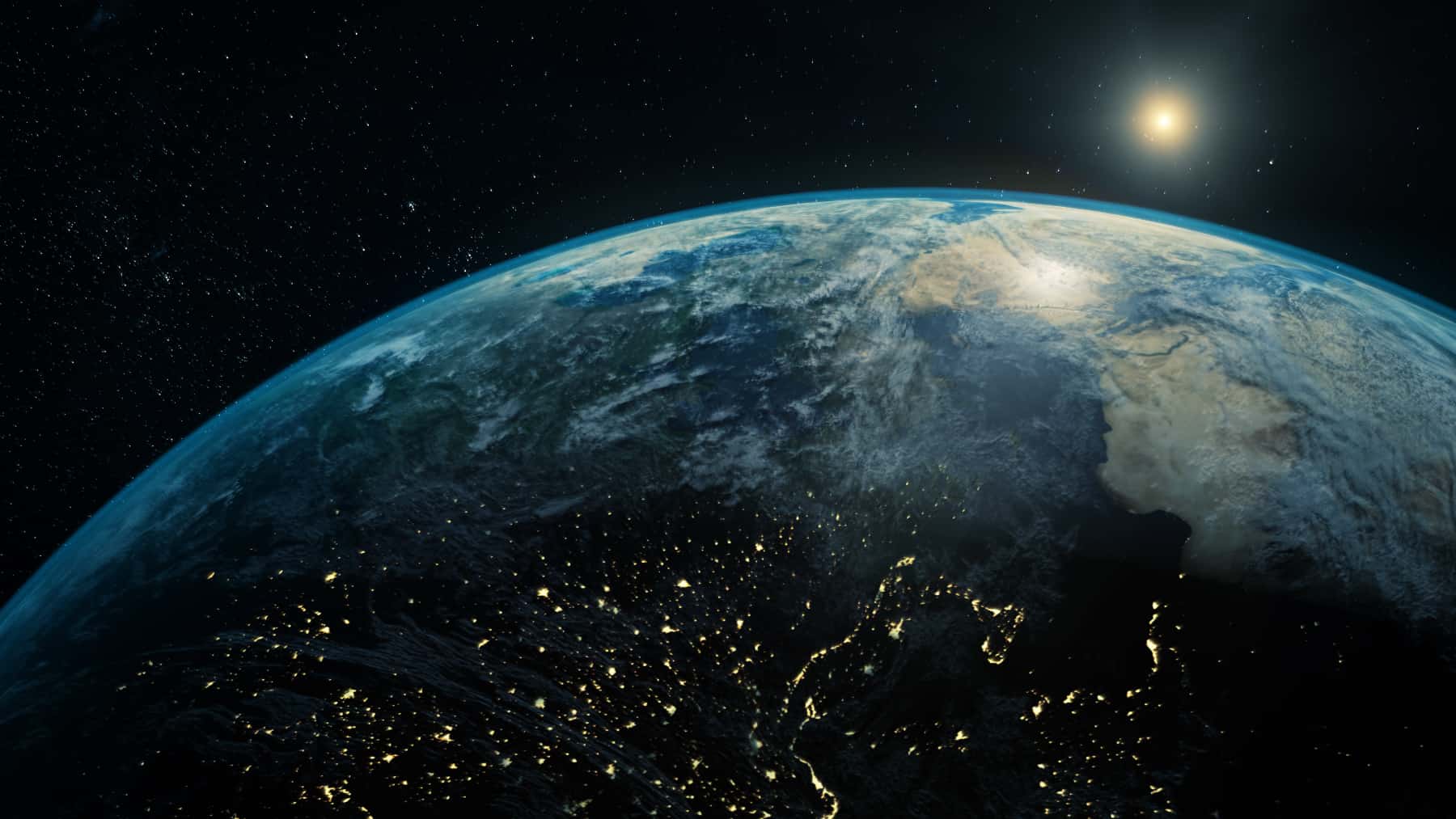 Vista de la Tierra desde el espacio con Europa iluminada por las luces de las ciudades durante la noche y el Sol en el horizonte.