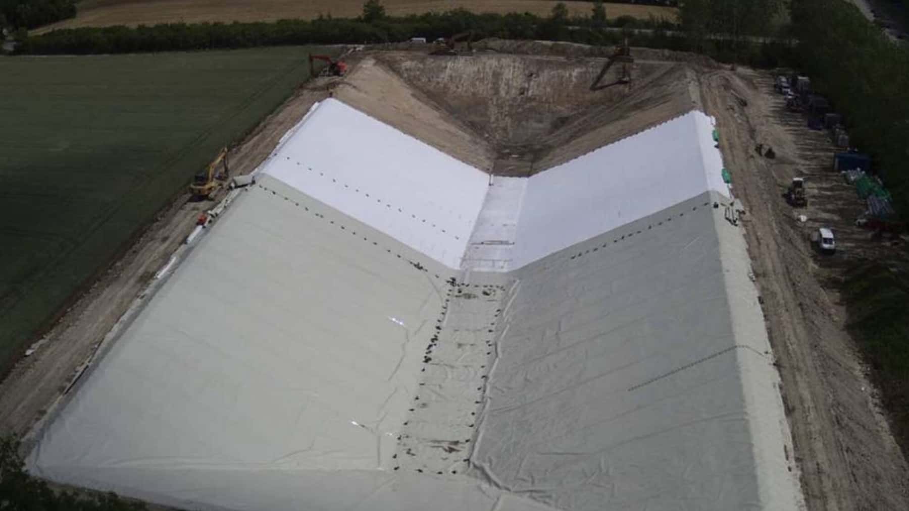 Vista aérea de una gran balsa impermeabilizada con lámina geotextil blanca durante su fase de construcción en una zona rural.