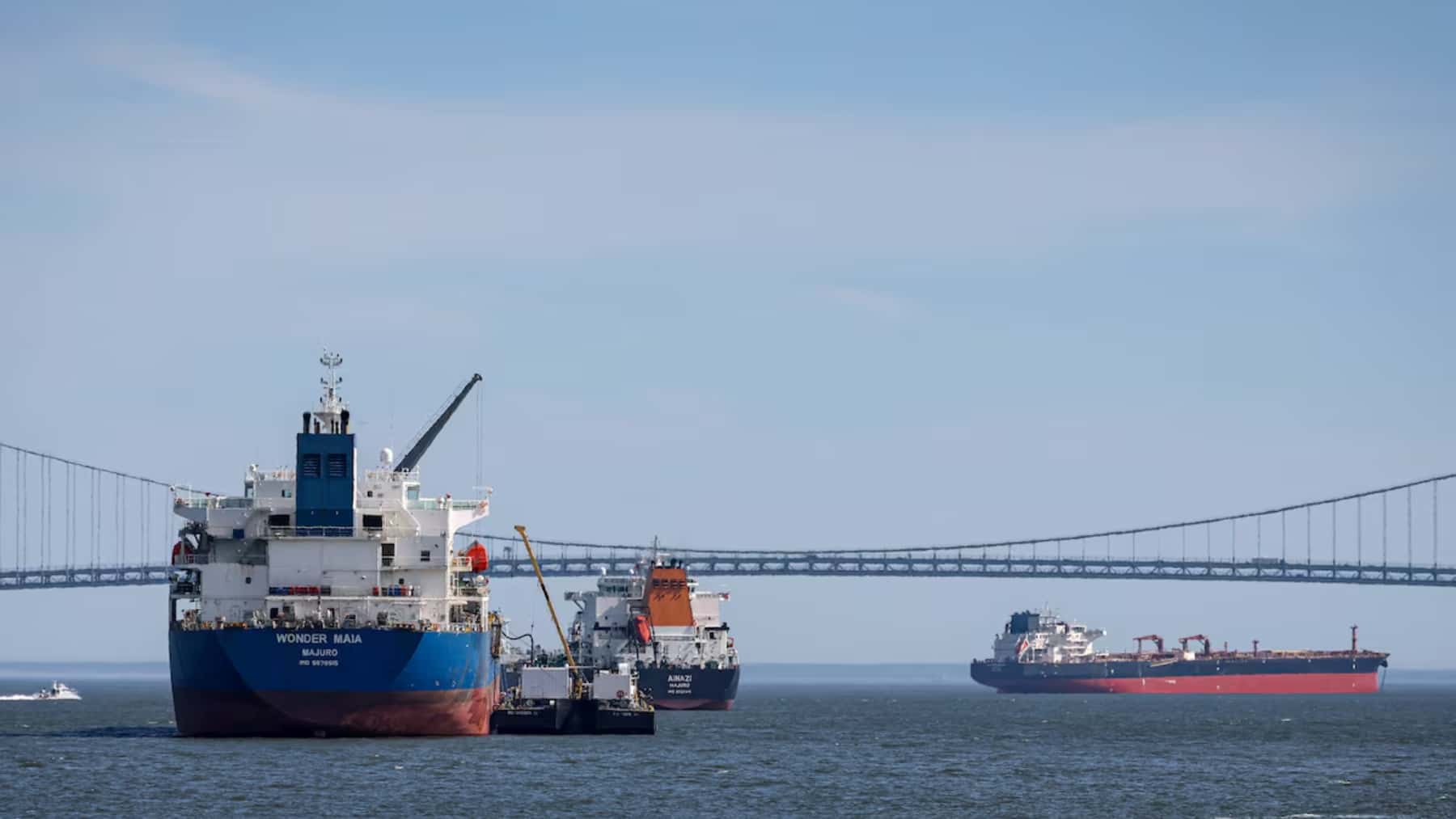 Varios barcos cargueros navegando junto a un gran puente sobre la bahía