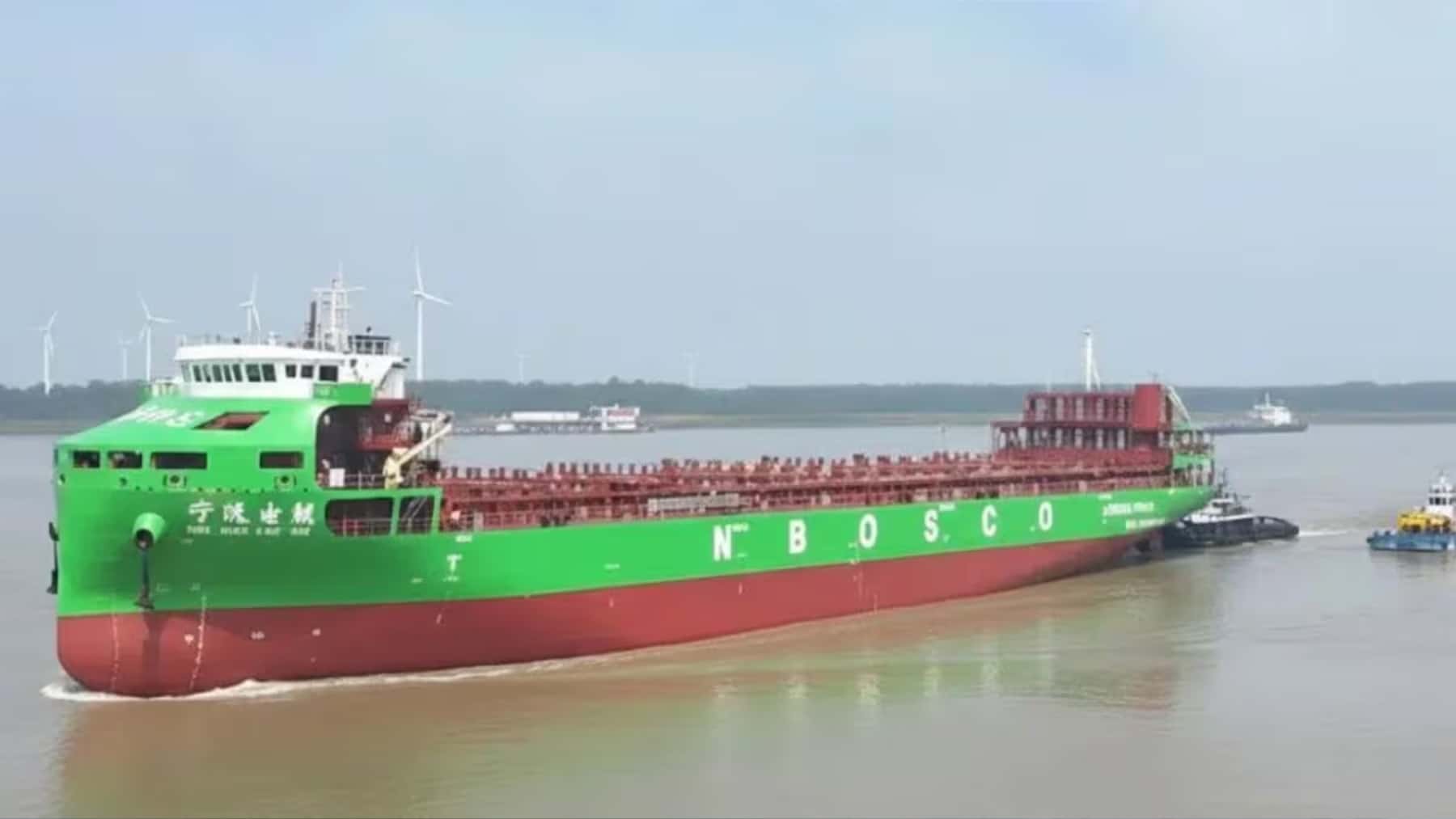 Buque carguero verde y rojo NBOSCO navegando por aguas portuarias con remolcadores junto al casco.