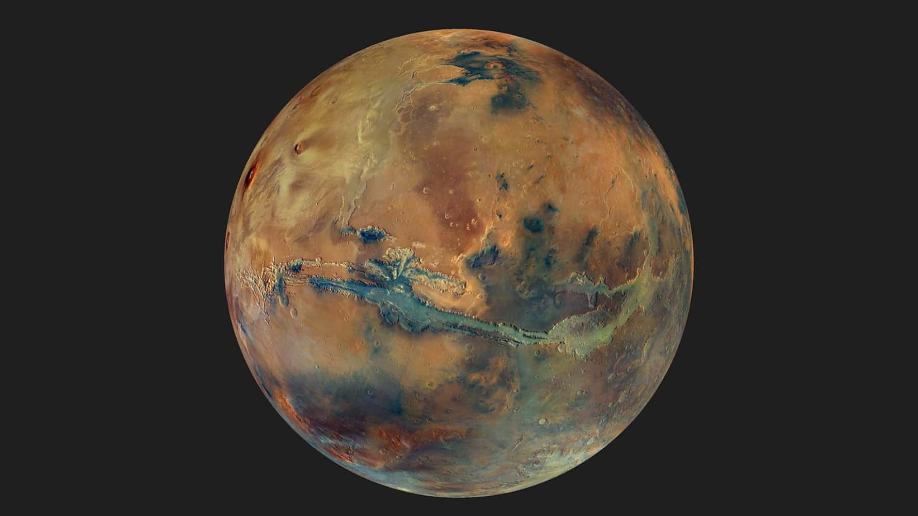 Imagen global del planeta Marte con detalles de su superficie en tonos ocres, azulados y oscuros sobre fondo negro.